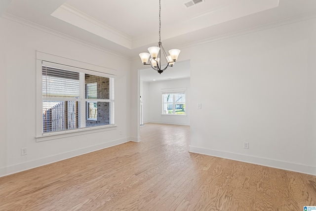 empty room with light hardwood / wood-style flooring, a tray ceiling, an inviting chandelier, and crown molding