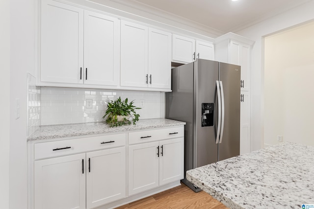 kitchen featuring light stone counters, stainless steel fridge, tasteful backsplash, white cabinetry, and light wood-type flooring