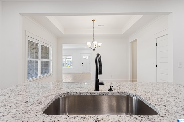 kitchen featuring hanging light fixtures, sink, light stone counters, and a raised ceiling