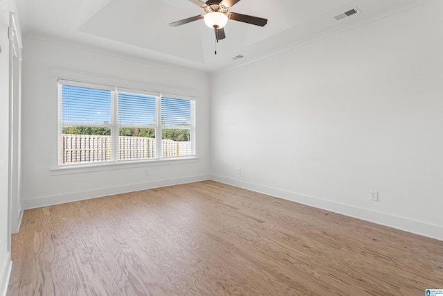 empty room featuring crown molding, light hardwood / wood-style floors, a tray ceiling, and ceiling fan