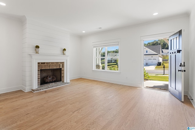 unfurnished living room with ornamental molding, a brick fireplace, and light wood-type flooring