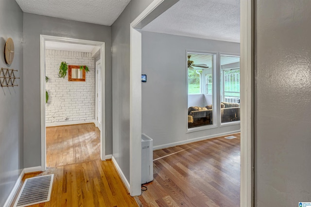 hall with a textured ceiling, light hardwood / wood-style floors, and brick wall