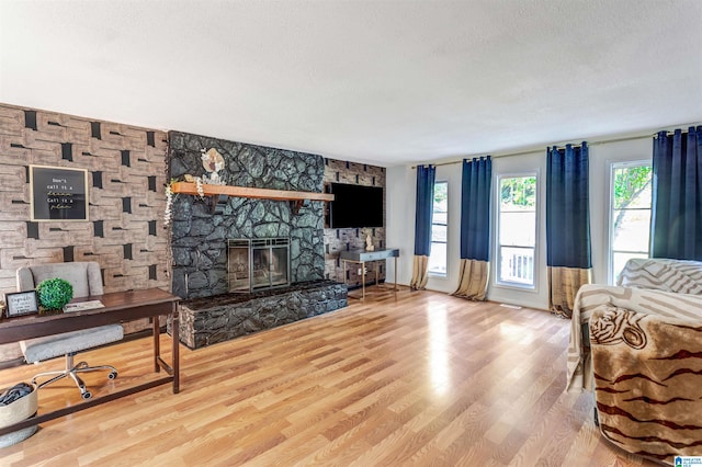 living room with a textured ceiling, wood-type flooring, and a stone fireplace