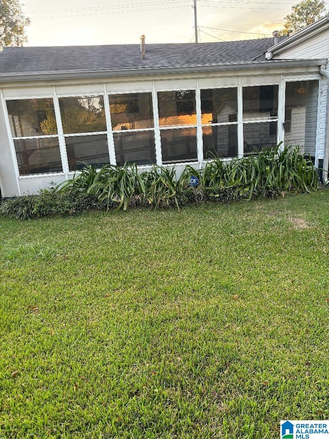 back house at dusk with a lawn and a sunroom