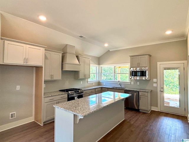 kitchen featuring light stone counters, a center island, dark wood-type flooring, custom range hood, and appliances with stainless steel finishes