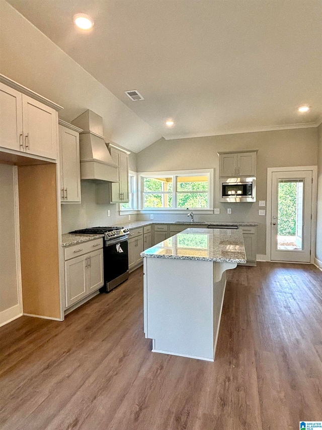 kitchen with appliances with stainless steel finishes, vaulted ceiling, a center island, custom exhaust hood, and light hardwood / wood-style flooring