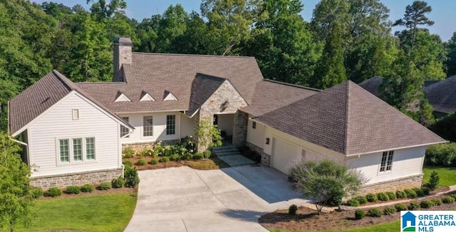 view of front facade with stone siding, an attached garage, a chimney, and driveway