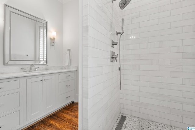 bathroom with wood-type flooring, tiled shower, and vanity