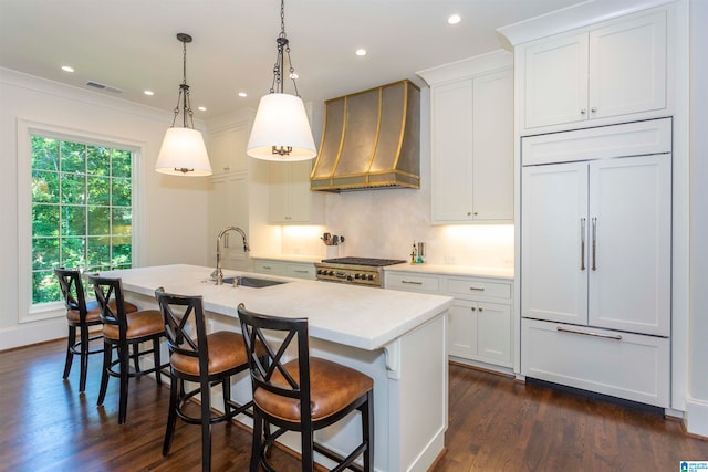 kitchen with white cabinets, custom exhaust hood, decorative light fixtures, a center island with sink, and sink