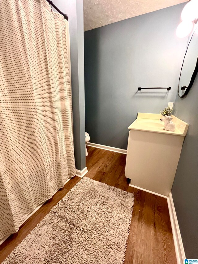 bathroom with vanity, a textured ceiling, a shower with shower curtain, hardwood / wood-style flooring, and toilet