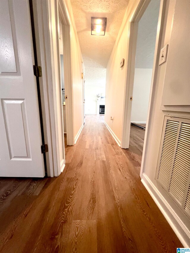 corridor with light wood-type flooring and a textured ceiling