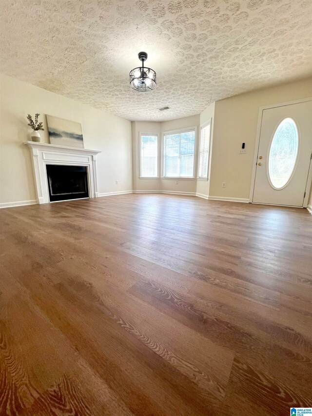 unfurnished living room featuring wood-type flooring, a textured ceiling, and a notable chandelier