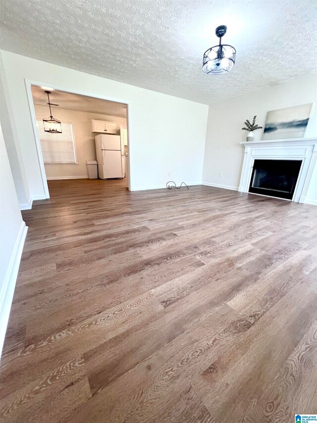 unfurnished living room with a textured ceiling, an inviting chandelier, and hardwood / wood-style floors