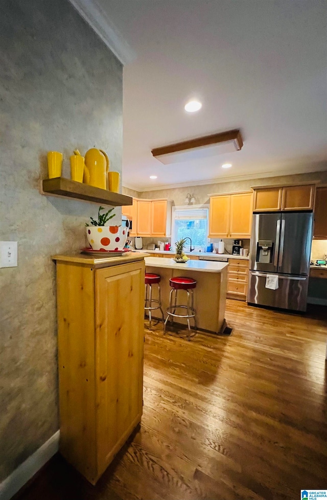 kitchen featuring a breakfast bar area, a kitchen island, stainless steel fridge with ice dispenser, hardwood / wood-style flooring, and sink