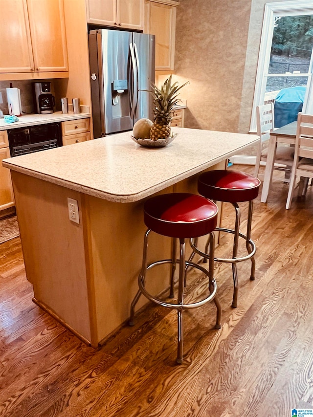 kitchen with stainless steel fridge, a center island, light wood-type flooring, and light brown cabinets