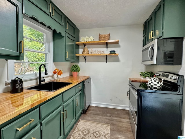 kitchen with sink, butcher block countertops, green cabinetry, light hardwood / wood-style flooring, and stainless steel appliances