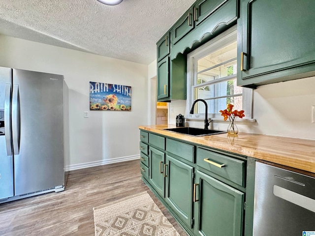 kitchen featuring stainless steel refrigerator, butcher block counters, light wood-type flooring, sink, and green cabinets