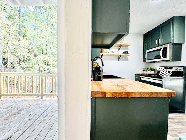 kitchen with green cabinetry, butcher block counters, stainless steel appliances, light wood-type flooring, and a textured ceiling