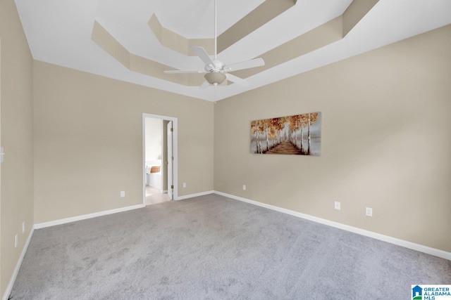 empty room featuring ceiling fan, a raised ceiling, and carpet flooring