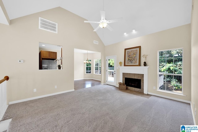 unfurnished living room featuring ceiling fan with notable chandelier, a tiled fireplace, light colored carpet, and high vaulted ceiling