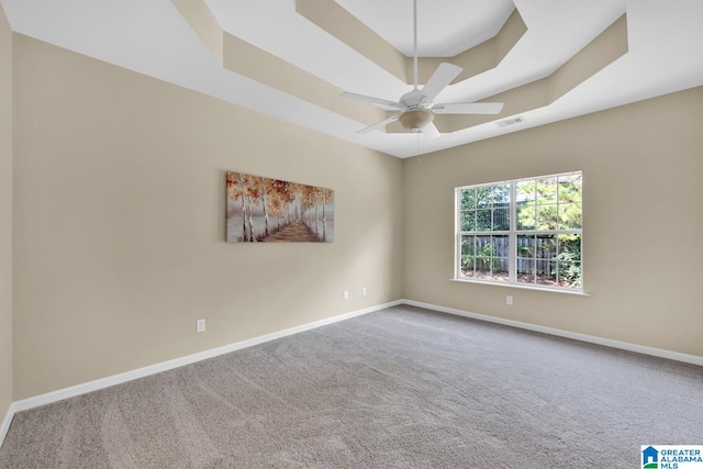 empty room with ceiling fan, a tray ceiling, and carpet flooring