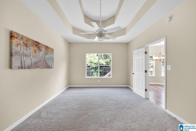 carpeted empty room with ceiling fan with notable chandelier and a raised ceiling