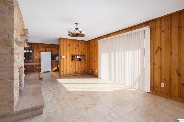 unfurnished living room featuring a notable chandelier and wood walls