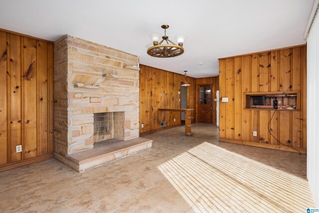 unfurnished living room featuring wooden walls, a chandelier, and a stone fireplace