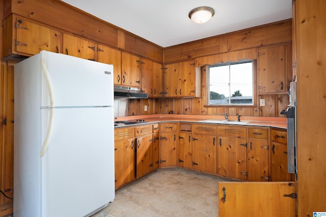 kitchen featuring wood walls, stainless steel gas cooktop, white fridge, and sink