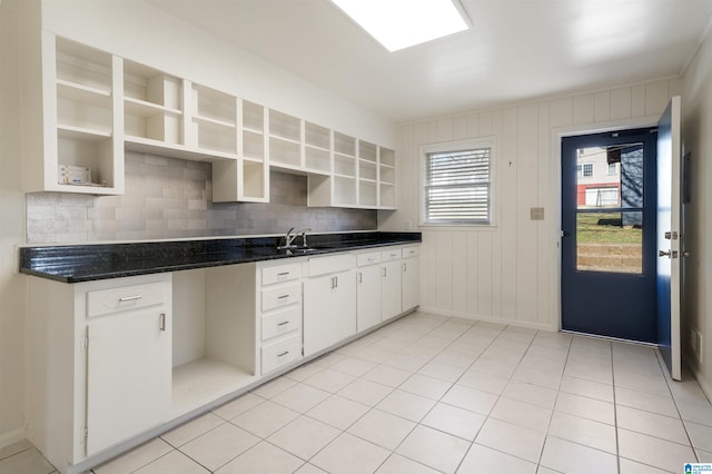 kitchen featuring wooden walls, backsplash, sink, and white cabinetry