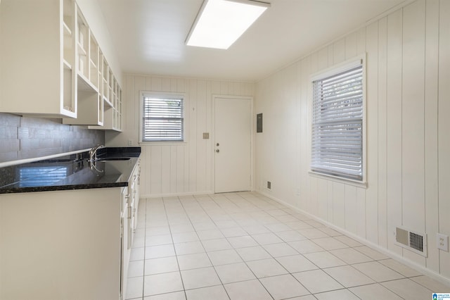 kitchen featuring light tile patterned flooring, sink, wooden walls, white cabinetry, and decorative backsplash