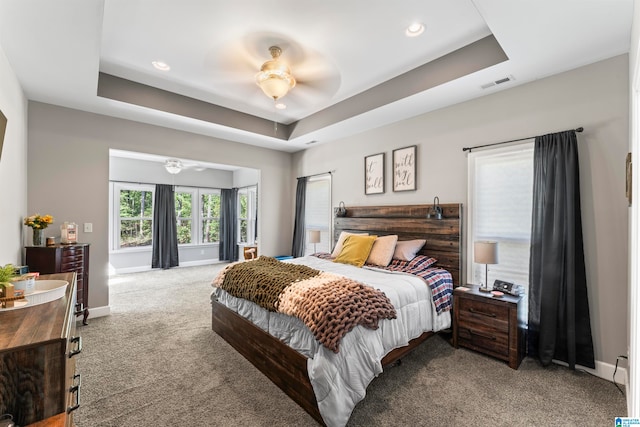 carpeted bedroom featuring ceiling fan and a raised ceiling