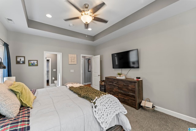 carpeted bedroom with ceiling fan, a tray ceiling, and ensuite bathroom