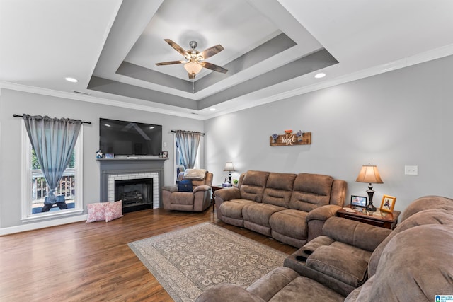 living room featuring ceiling fan, a brick fireplace, dark wood-type flooring, a tray ceiling, and crown molding