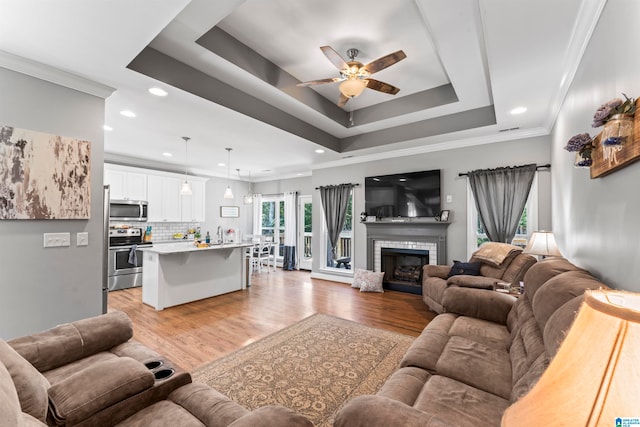 living room with a brick fireplace, light wood-type flooring, ornamental molding, and ceiling fan