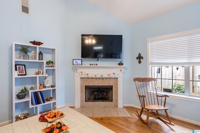 living room with a tiled fireplace, light hardwood / wood-style flooring, and lofted ceiling