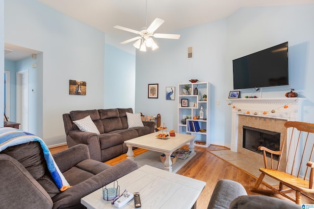 living room featuring a tile fireplace, ceiling fan, vaulted ceiling, and light wood-type flooring