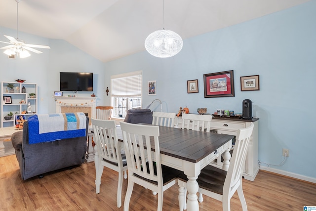 dining area with ceiling fan with notable chandelier, vaulted ceiling, and light hardwood / wood-style flooring