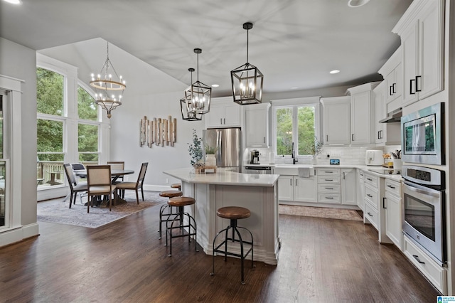 kitchen with white cabinetry, a kitchen island, appliances with stainless steel finishes, a healthy amount of sunlight, and decorative light fixtures