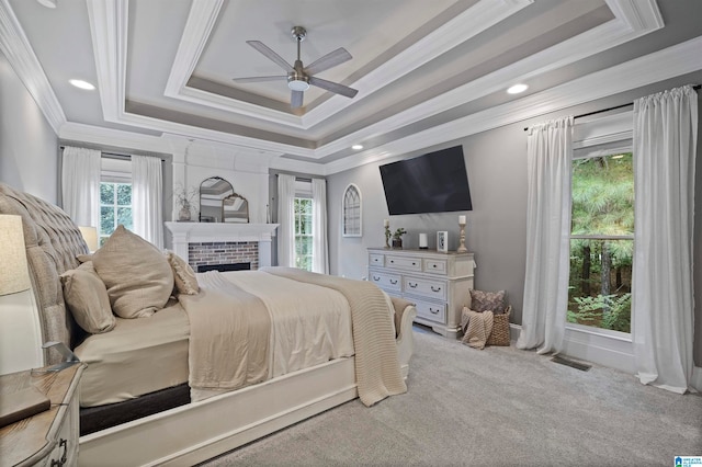 carpeted bedroom featuring a brick fireplace, a tray ceiling, ceiling fan, and crown molding