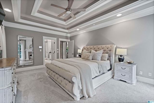 carpeted bedroom with a brick fireplace, a raised ceiling, crown molding, ceiling fan, and ensuite bathroom