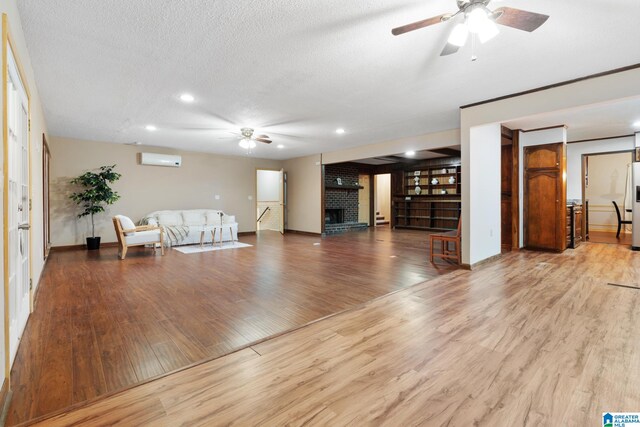 living room with a wall unit AC, ceiling fan, a textured ceiling, light wood-type flooring, and a brick fireplace