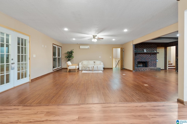 unfurnished living room featuring french doors, light hardwood / wood-style flooring, a textured ceiling, a fireplace, and ceiling fan