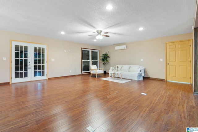 unfurnished living room featuring french doors, a wall mounted AC, wood-type flooring, a textured ceiling, and ceiling fan