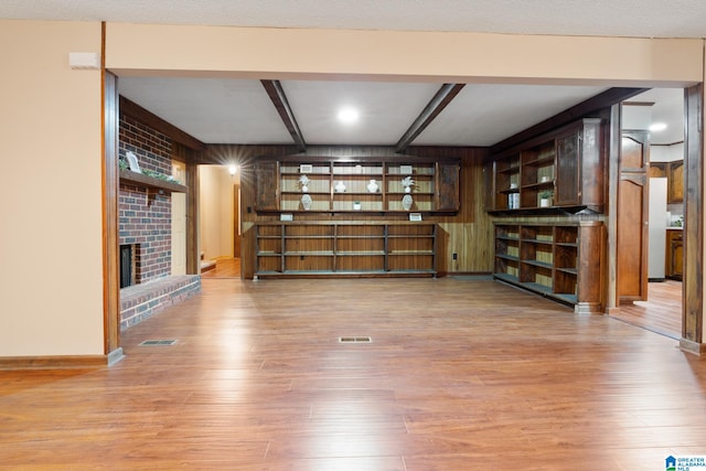 unfurnished living room with beamed ceiling, light hardwood / wood-style flooring, a fireplace, and a textured ceiling