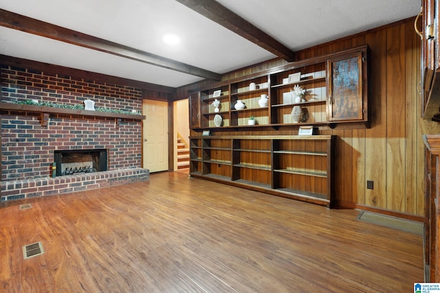 unfurnished living room featuring beam ceiling, a brick fireplace, wooden walls, and hardwood / wood-style floors