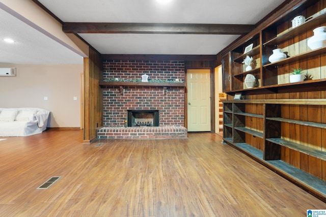 unfurnished living room featuring an AC wall unit, beamed ceiling, light hardwood / wood-style flooring, and a fireplace