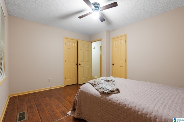 bedroom featuring dark wood-type flooring, ceiling fan, a textured ceiling, and two closets