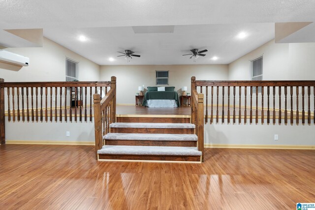 staircase featuring baseboards, ceiling fan, a wall mounted AC, and wood finished floors