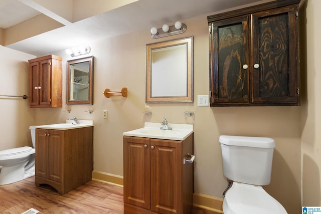bathroom with a sink, toilet, baseboards, two vanities, and wood finished floors